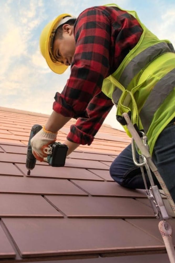 A man in a safety vest and hard hat diligently working on a roof in Dallas, TX, showcasing professional roofing services.