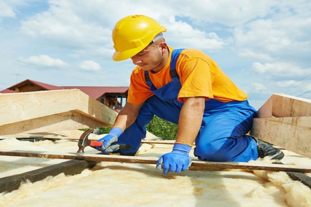 A man wearing blue overalls works on a roof, highlighting a roof repair service in Dallas, TX.