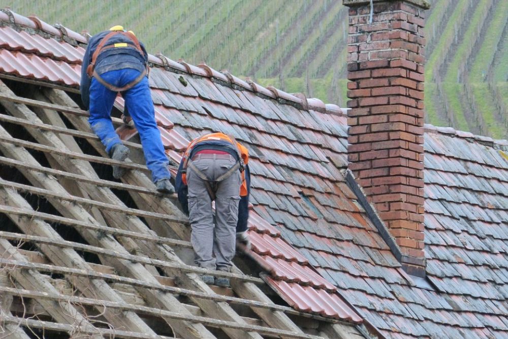 Two men repairing a roof in Dallas, TX, with a brick chimney in the background, showcasing professional roofing service.