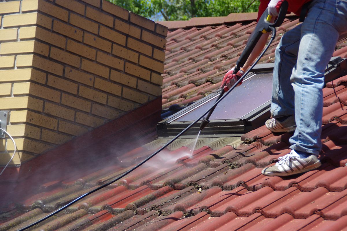 A man using a pressure washer to clean a metal roof, showcasing effective roof maintenance techniques.