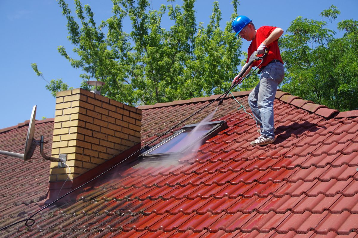 A man using a pressure washer to clean a roof, demonstrating professional roof cleaning techniques.